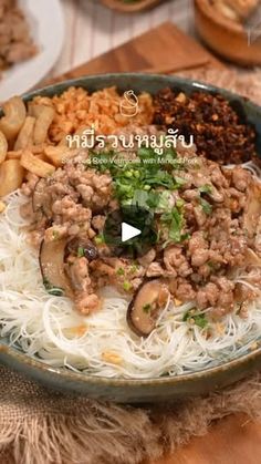 a bowl filled with noodles and meat on top of a wooden table next to other food items