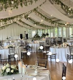 the inside of a wedding reception with white linens and greenery hanging from the ceiling