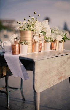 a table topped with lots of vases filled with white and pink flowers next to a wooden bench