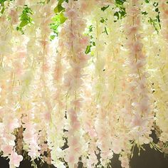 pink and white flowers hanging from the ceiling in front of a tree with green leaves