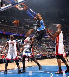 a basketball player jumping up into the air to dunk a ball in front of two other players