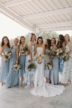 a group of women standing next to each other wearing dresses and holding bouquets in their hands