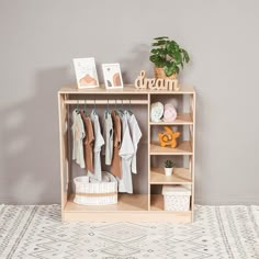 a wooden shelf filled with clothes next to a potted plant on top of a rug