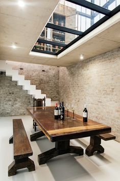 a wooden table sitting under a skylight next to a set of stairs with wine bottles on it