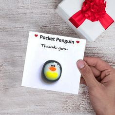 a hand holding a card with a penguin on it next to a gift box that says pocket penguin thank you