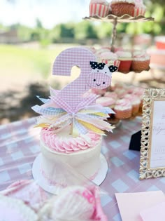 a table topped with cupcakes and cakes covered in pink frosting next to a sign