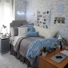 a bedroom with white brick walls and grey bedding, blue throw pillows and pictures on the wall