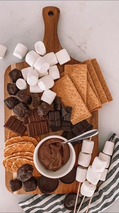 a cutting board with marshmallows, chocolate and graham crackers on it