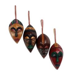 three wooden masks hanging from strings on a white wall, each with different designs and colors