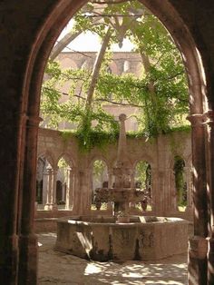 an archway leading into a courtyard with a fountain in the center and trees growing all around