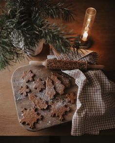 cookies on a cutting board next to a lit candle and christmas tree branch in the background