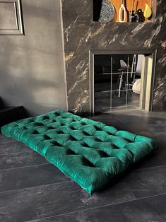 a green futon mattress sitting on the floor in front of a stone wall and fireplace