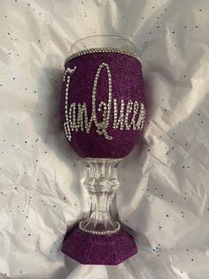 a purple wine glass with the word queen on it sitting on a white tablecloth