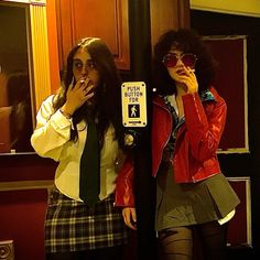 two women standing next to each other in front of a parking meter with their hands on their mouths