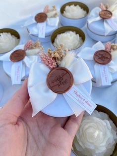 a hand holding a small white box filled with cupcakes on top of a table