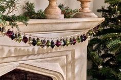 a christmas tree is next to a fireplace with ornaments on it and a garland hanging from the mantel