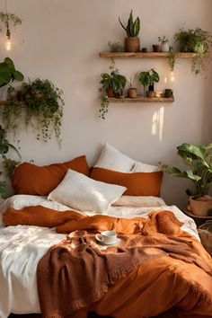 a bed covered in lots of pillows and blankets next to potted plants on the wall