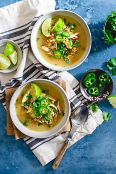 two bowls of chicken soup with limes, cilantro and green onions on a blue background