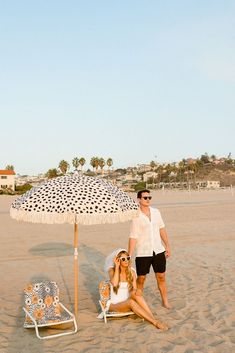 a man and woman sitting under an umbrella on the beach