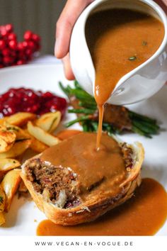 a person pouring gravy on top of a meatloaf roll with french fries