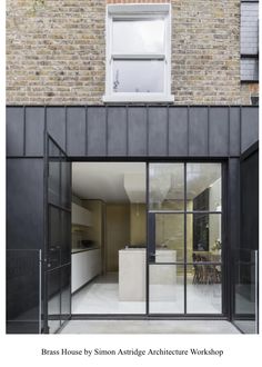 an open glass door leading to a kitchen and dining area in front of a brick building