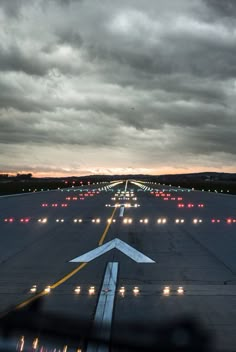 an airport tarmac with lights on the runway at night and dark clouds in the sky