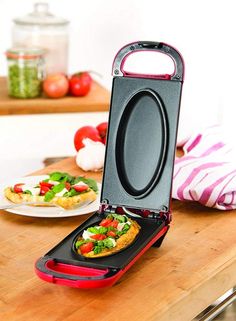 an open lunch box with food inside on a wooden table next to plates and utensils