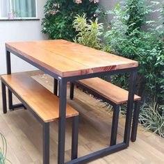 a wooden table with two benches in front of some plants and bushes on the ground