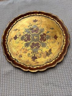 a decorative gold plate sitting on top of a gray cloth covered floor next to a wall