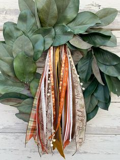 a wreath with green leaves and ribbons hanging from it's side on a white wooden wall