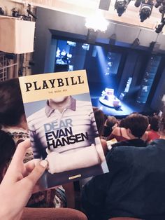 a person holding up a playbill book in front of a crowd at a concert