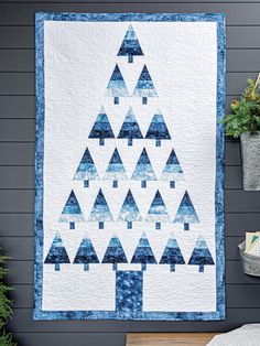 a blue and white christmas tree quilt hanging on the wall next to a potted plant