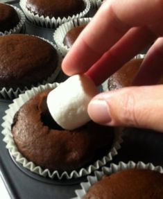 a hand is dipping marshmallows into chocolate cupcakes