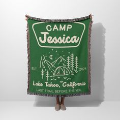 a woman standing in front of a green tapestry with the camp tescha logo on it