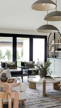 a living room filled with lots of furniture next to tall windows and potted plants