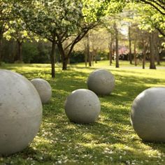 several cement balls sitting in the grass near trees