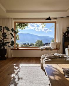 a bedroom with a large open window overlooking the mountains and valleys in the distance is furnished with natural wood flooring