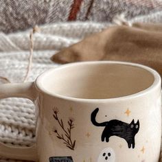 a white coffee cup with black cats and ghostes on it sitting on a blanket