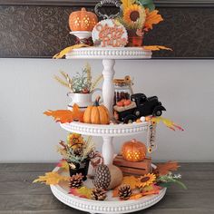 a three tiered cake stand with pumpkins, gourds and other decorations