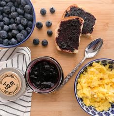 blueberries, bread and jam on a wooden table with spoons next to it