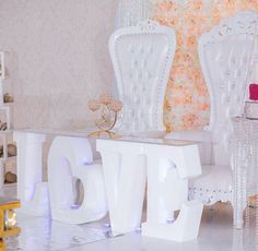 a room with white furniture and pink flowers on the wall behind it is a love sign made out of plastic letters