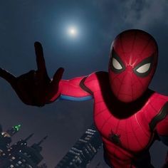 the spider - man is standing in front of a city at night with his hands up