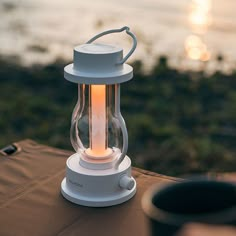 a white lantern sitting on top of a table next to the ocean at sunset or dawn