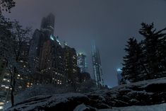 the city is lit up at night with snow on the ground and tall buildings in the background