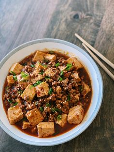 a bowl filled with meat and vegetables next to chopsticks on a wooden table