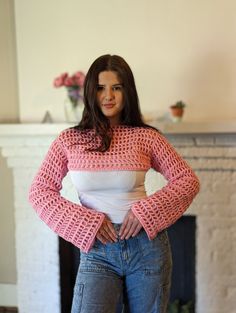 a woman standing in front of a fireplace wearing jeans and a pink knitted sweater