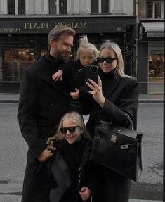 a man, woman and child taking a selfie on the street with their cell phone