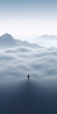 a lone person standing in the middle of a foggy mountain range with mountains in the distance