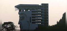 a tall white building with a face on it's side and trees in the background