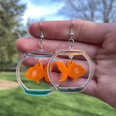 "Pair of Goldfish in a Bowl Dangle Earrings * Created from 3mm thick acrylic on a professional grade laser * Each earring is 2 pieces with the goldfish floating inside the bowl. * Each fishbowl is 1-1/2\" tall and 1-1/2\" wide. * A bit under 2-1/2 inches long from top of hook to bottom of the fishbowl * Extremely lightweight - each individual earring weighs less than an ounce * Nickel Free and Hypoallergenic * Super cute and trendy!" Handmade Funky Dangle Earrings, Quirky Hypoallergenic Dangle Jewelry, Weird Earrings Aesthetic, Weird Core Earrings, Novelty Everyday Dangle Earrings, Goldfish In A Bowl, Cardboard Earrings, Goldfish Earring, Silly Earrings